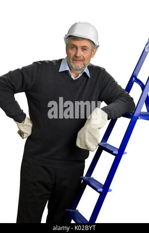 Auftragnehmer in Helm und Handschuhe stützte sich auf eine Leiter. Ausgereifte Konstruktion Supervisor in weißen Helm und Handschuhe lehnte sich auf Leiter, weiße backgroun Stockfoto