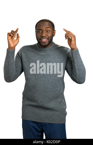 Lächelnd Mann die Hände und Zeigefinger. Positive dunkelhäutigen Mann in lässiger Pullover heben die Hände in der Nähe von Kopf. Mimik und Körpersprache. Stockfoto