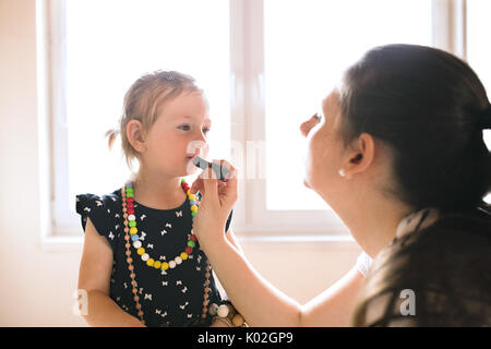 Mutter Malerei Lippen ihre süsse kleine Tochter mit Lippenstift. Stockfoto