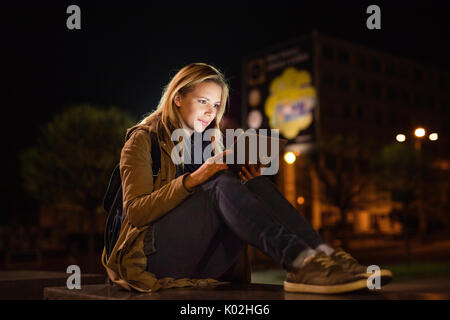 Frau in der Stadt bei Nacht Holding Tablet, etwas zu lesen. Stockfoto