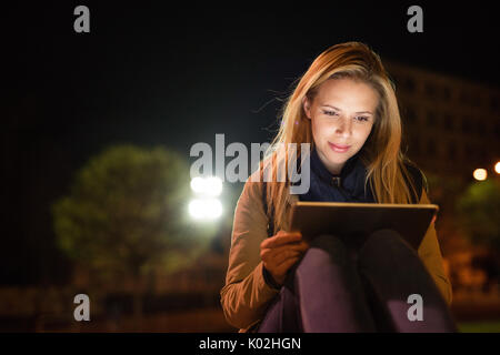 Frau in der Stadt bei Nacht Holding Tablet, etwas zu lesen. Stockfoto