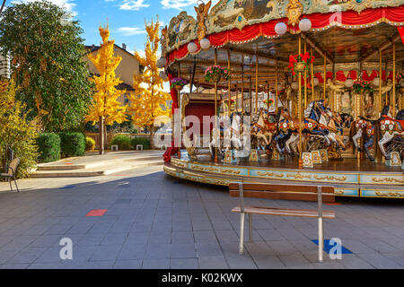 Bank vor Merry-go-round mit Pferden als Bäume mit gelben Blätter auf Hintergrund im Herbst in Alba, Italien. Stockfoto