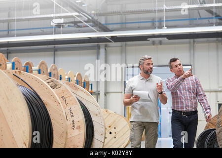 Männliche Vorgesetzte und Mitarbeiter mit Zwischenablage entlang Spulen in Fiber Optik Factory Stockfoto