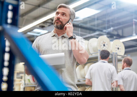 Männliche Supervisor mit Zwischenablage Gespräch am Handy in Fiber Optik Factory Stockfoto