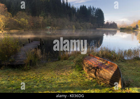 Ein umgedrehter alten hölzernen Boot liegend auf Gras auf einem nebligen Morgen mit Reflexion, Loch Ard, Schottland Stockfoto