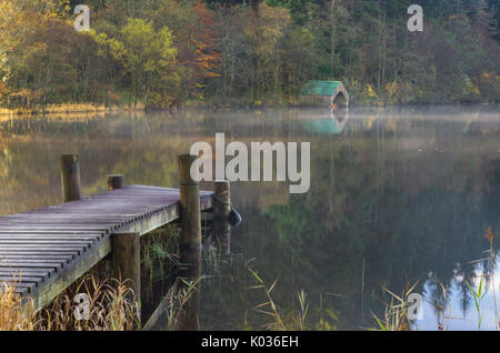 Holzsteg und Bootshaus auf einem nebligen Morgen mit Reflexion, Loch Ard, Schottland Stockfoto