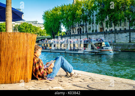 Ein Mann liest während einer Bootsfahrt auf der Seine auf einem schönen Sommern' Tageskarten Stockfoto