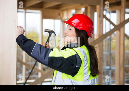 Lächelnd weibliche Tischler Hämmern Nagel in Holz am Standort Stockfoto