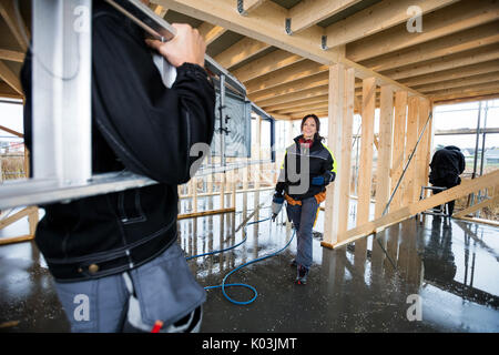 Frau Carpenter lächelnd Während männliche Kollegen die Leiter Stockfoto