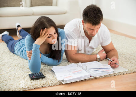 Besorgt Junges Paar Liegen auf dem Teppich, Ihre Rechnungen zu Hause Berechnung Stockfoto