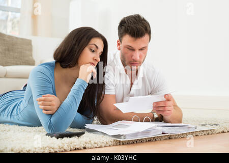 Besorgt Junges Paar Liegen auf dem Teppich, Ihre Rechnungen zu Hause Berechnung Stockfoto