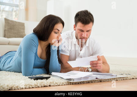 Besorgt Junges Paar Liegen auf dem Teppich, Ihre Rechnungen zu Hause Berechnung Stockfoto