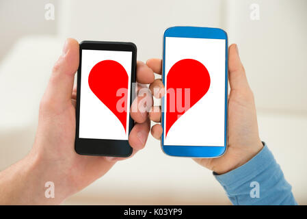 In der Nähe von ein paar Hand Handy mit der Hälfte Rotes Herz Symbol Stockfoto