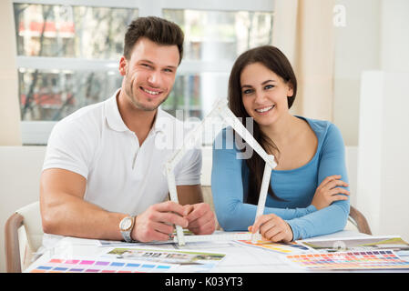 Glückliches Paar sitzt auf Stuhl Holding Modell Haus Aus Messung Klebeband Stockfoto