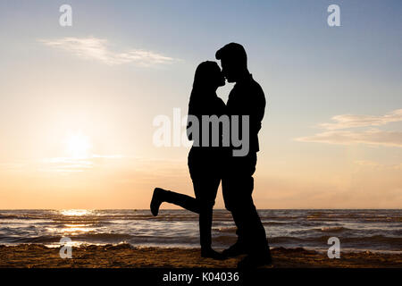 Silhouette der liebenden Paar an der Küste bei Sonnenuntergang stehend Stockfoto