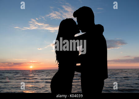 Silhouette von Paar küssen Vor Meer am Strand bei Sonnenuntergang Stockfoto