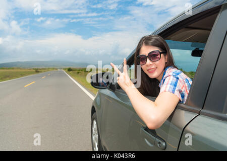 Hübsche Studentin drive Stoppen am Dorf am Straßenrand im Auto Gesicht sitzen zu Kamera und Sieg Geste glücklich Urlaub genießen. Stockfoto