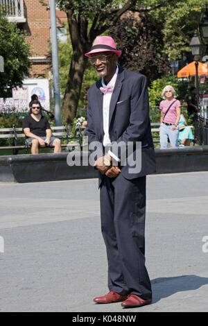 Ein gut gekleideter älterer Mann im Anzug mit einem rosa Hut, d Fliege und hankie beobachten Darsteller in den Washington Square Park in Manhattan, New York City Stockfoto