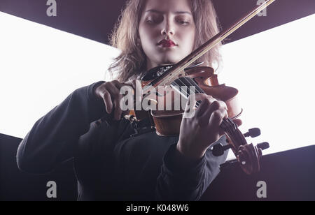 Schöne junge Frau spielt die Geige auf dunklem Hintergrund Stockfoto