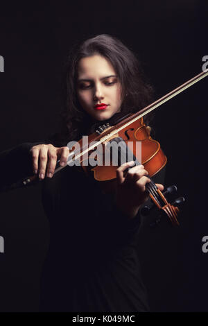 Schöne junge Frau spielt die Geige auf dunklem Hintergrund Stockfoto