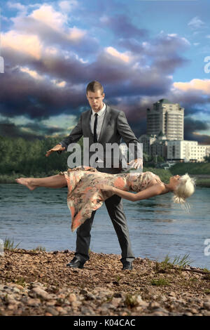 Ein hübscher zuversichtlicher Mann hält eine junge Dame, die in der Luft schweben. Stockfoto