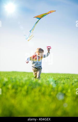 Kleiner Junge spielt mit seinem Kite in einem grünen Feld. Stockfoto