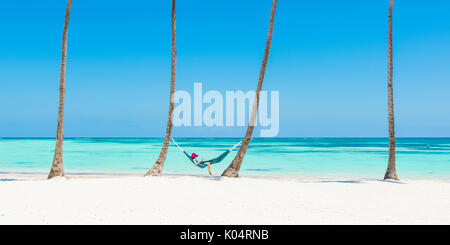 Juanillo Strand (Playa Juanillo), Punta Cana, Dominikanische Republik. Entspannen Sie sich auf einer Hängematte an einem palmengesäumten Strand (MR) Frau. Stockfoto