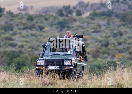 Safari Touristen stehen Ihre lange Teleobjektive auf die Tierwelt aus einer typischen offenen Jeep Safari in die Masai Mara, Kenia zu trainieren Stockfoto