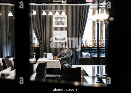 Erfolgreicher Geschäftsmann im Anzug Arbeiten am Laptop sitzen am Tisch in der Lobby Stockfoto