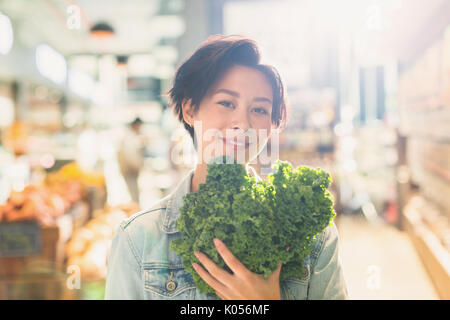 Portrait lächelnde junge Frau mit frischen Grünkohl in Lebensmittelgeschäft Markt Stockfoto