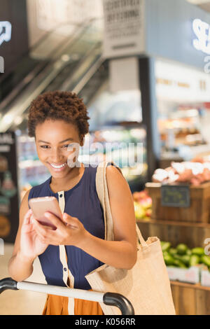 Lächelnde junge Frau mit Handy in Lebensmittelgeschäft Markt Stockfoto