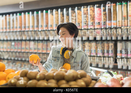 Junge Frau mit Kopfhörern Einkaufen, Holding orange im Markt Stockfoto