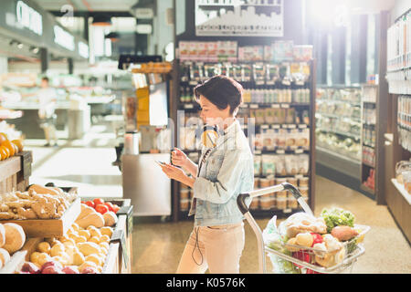 Junge Frau mit Kopfhörern über Handy, Einkaufen auf dem Markt Stockfoto