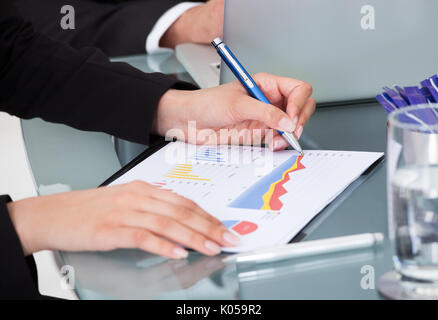 Zugeschnittenes Bild der Unternehmerin schreiben auf Graph am Schreibtisch im Büro Stockfoto