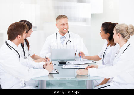 Lächelnd männlicher Arzt diskutieren mit Kollegen am Schreibtisch, in der Klinik Stockfoto
