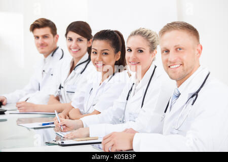 Portrait von zuversichtlich Ärzte in einer Reihe sitzen am Schreibtisch Stockfoto