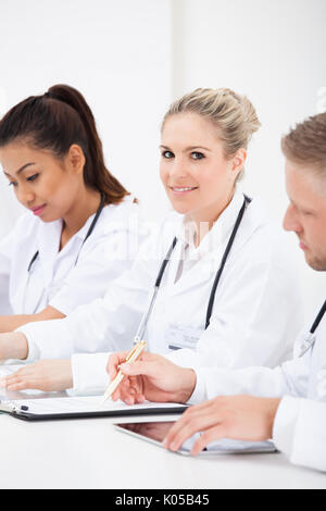 Ärzteteam schreiben am Schreibtisch sitzend in einer Reihe Stockfoto