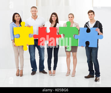 In voller Länge Portrait von zuversichtlich Geschäftsleute Beitritt Puzzleteile im Büro Stockfoto