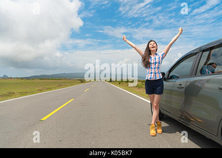 Schlanke elegante weibliche Reisende stoppen Auto auf Asphalt am Straßenrand und neben dem Auto erhobenen Händen genießen Landschaft Landschaft. Stockfoto