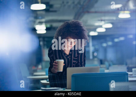 Geschäftsfrau, die spät am Laptop, Kaffee trinken in dunklen Büro Stockfoto