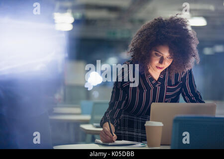 Fokussierte Geschäftsfrau spät am Laptop arbeiten, Notizen in dunklen Büro Stockfoto