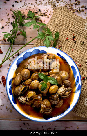 High-Angle Schuss eine Keramikschale mit spanischen Caracoles de Salsa, gekochte Schnecken in Soße, auf einem rustikalen Holztisch Stockfoto