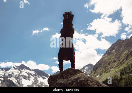 Mann tun, komplexe Yogaübung Kopfstand. Erstaunlich Yoga Landschaft in herrlicher Bergwelt. Gefährliche stunts Traceur stehend auf seine Hände auf den Edge o Stockfoto