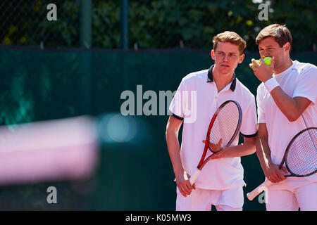 Junge männliche Tennis Doubles Spieler sprechen, strategizing Stockfoto