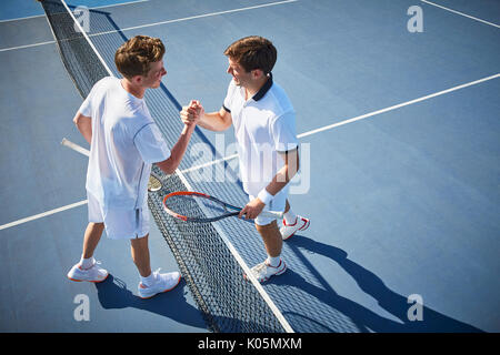 Jungen männlichen Tennisspieler handshaking am Tennis net auf sonnigen blauen Tennisplatz Stockfoto