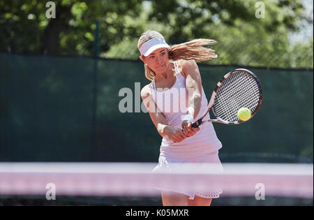 Entschlossene junge weibliche Tennisspieler Tennis spielen, den Ball schlagen an sonnigen Tennisplatz Stockfoto