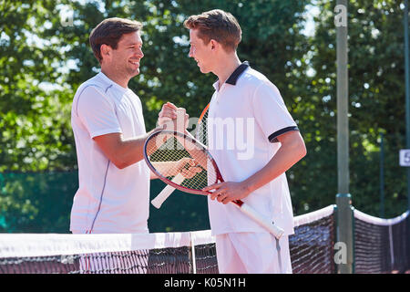 Lächelnden jungen männlichen Tennisspieler handshaking in sportsmanship über Netz auf dem Tennisplatz Stockfoto