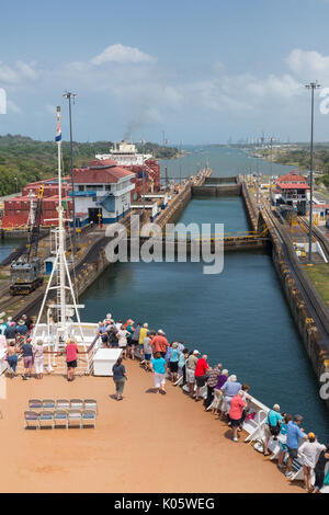 Panama Canal, Panama. Die Passagiere an Deck zusehen, wie Schiff Transite drei Ebenen von Sperren auf dem Weg in die Karibik. Auf der linken Seite, Container schiff nach Süden. Stockfoto