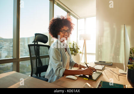 Portrait von Kreative junge Frau arbeiten im Büro mit Grafik Tablett. Afrikanische Frauen Designer an ihrem Schreibtisch arbeiten und lächelnd. Stockfoto