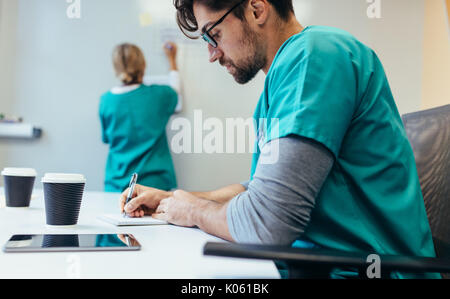 Seitenansicht des healthcare Arbeiter im Krankenhaus Sitzungssaal Sitzung Notizen mit weiblichen im Hintergrund. Stockfoto